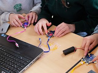 Schülerinnen an einem Tisch drücken Tasten an technischen Geräten