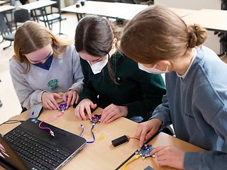 Drei Schülerinnen programmieren eine künstliche Intelligenz mithilfe des Mikro-Computers Calliope mini.