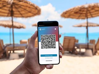 Smartphone with QR code in front of beach umbrellas.