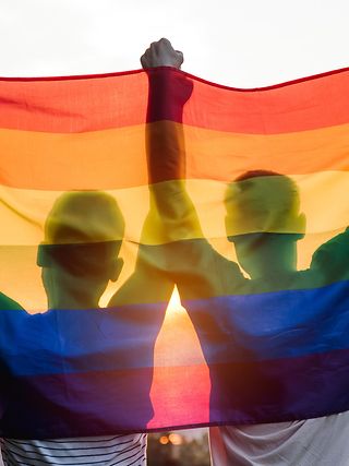 Two people holding a rainbow flag in the air 