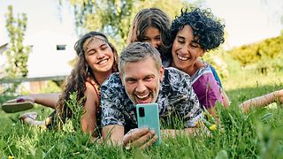 Family lying on the grass taking a selfie with a smartphone.