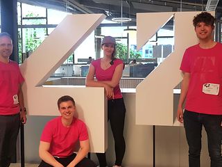 vier T-Systems Mitarbeiter stehen vor dem Wolfburg42 Logo