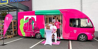 In der geöffneten Tür eines magentafarbenen Trucks steht ein vierköpfiges Beratungsteam und winkt dem Betrachter zu. 