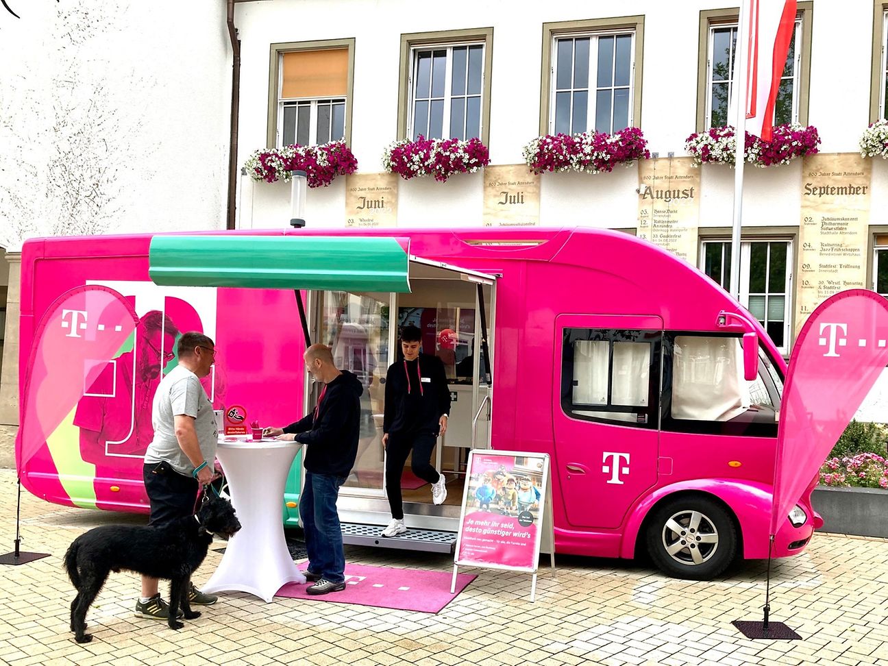 Ein Telekom Mitarbeiter berät einen Kunden mit Hund an einem Stehtisch vor dem Telekom Truck.