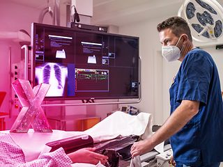Arzt steht am Krankenbett mit diversen Monitoren im Hintergrund