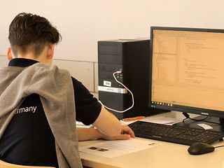 Junger sitz an einem Schreibtisch mit einem PC und schreibt einen Code