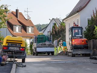 Baufahrzeuge und mit Erdarbeiten beschäftigte Arbeiter in einer Wohnstraße.