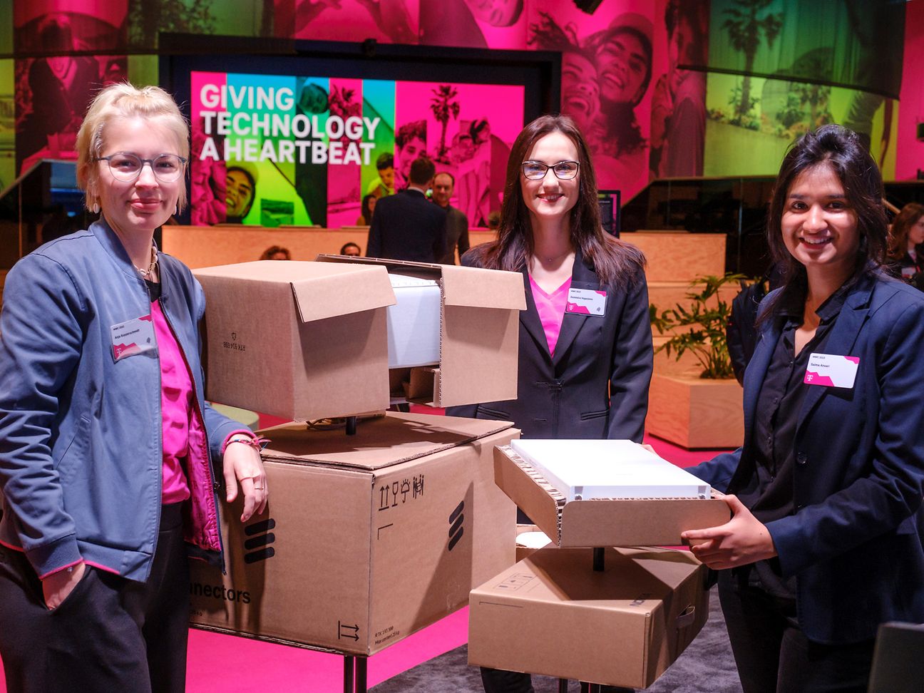 MWC Barcelona 2023 (© DTAG) Three female employees, cardboard boxes in between, belonging to their showcase.