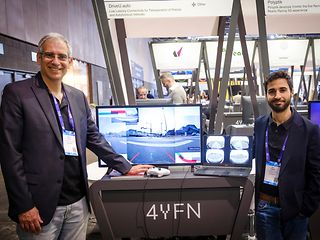 Two men demonstrate an application for remote vehicle solutions on a screen, with a street view livestreamed on the screen.