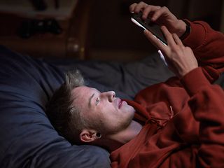 Junger Mann liegt auf dem Bett und schaut in sein Smartphone