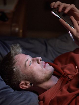 Junger Mann liegt auf dem Bett und schaut in sein Smartphone