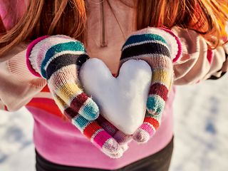 Zwei Hände mit Handschuh halten ein Herz aus Schnee
