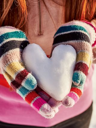 Zwei Hände mit Handschuh halten ein Herz aus Schnee