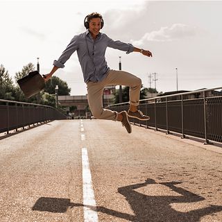 A man with headphones jumps happily into the air on a street.