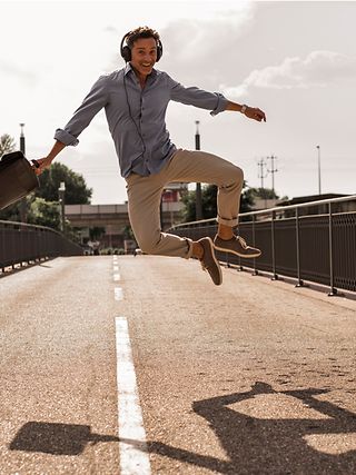 A man with headphones jumps happily into the air on a street.