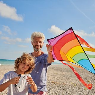 Father and child are flying a kite on the beach.