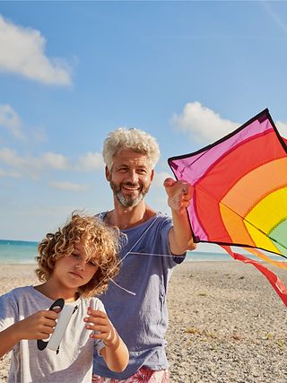 Father and child are flying a kite on the beach.