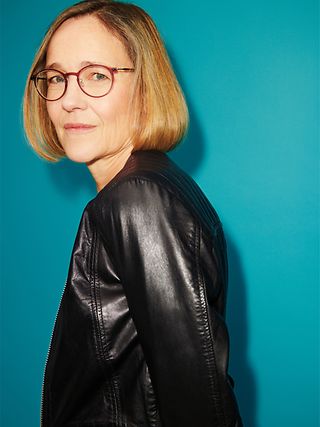 A woman wearing glasses looks over her shoulder into the camera.