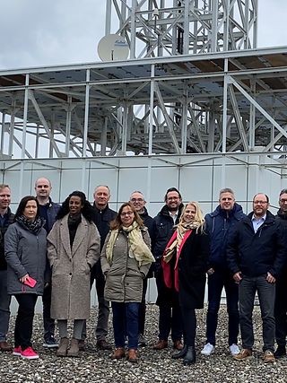 Die Besuchergruppe steht auf dem Dach des Gebäudes vor der Antenne.