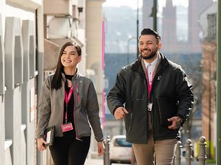 Ein Mann und eine Frau in Dienstkleidung der Telekom gehen eine Straße entlang. 