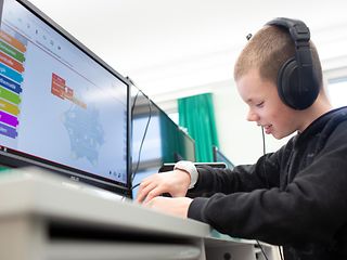 Ein junger Schüler sitzt vor dem PC und lernt Coden und Programmieren