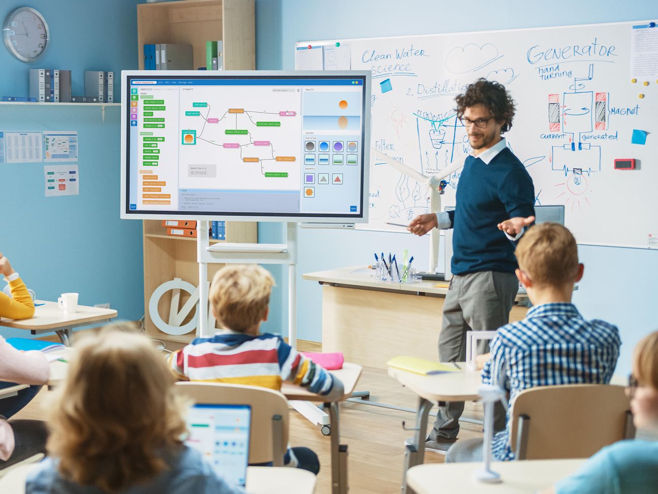 Lehrer steht vor der Klasse an einer digitalen Tafel.
