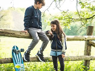 Ein Junge und ein Mädchen draußen in der Natur. Das Mädchen telefoniert über ihre Smartwatch.