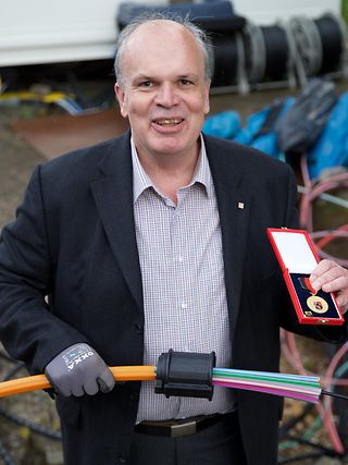 Michael Guthart hält seine Verdienstmedaille sowie ein Glasfaserbündel in der Hand
