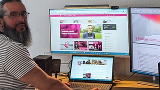  Hasan Kökcü stands in front of his desk with his laptop and two large screens