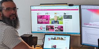  Hasan Kökcü stands in front of his desk with his laptop and two large screens