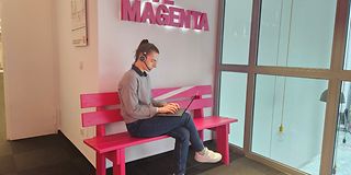 A trainee wearing a headset sits on a bench with a laptop in her lap, typing