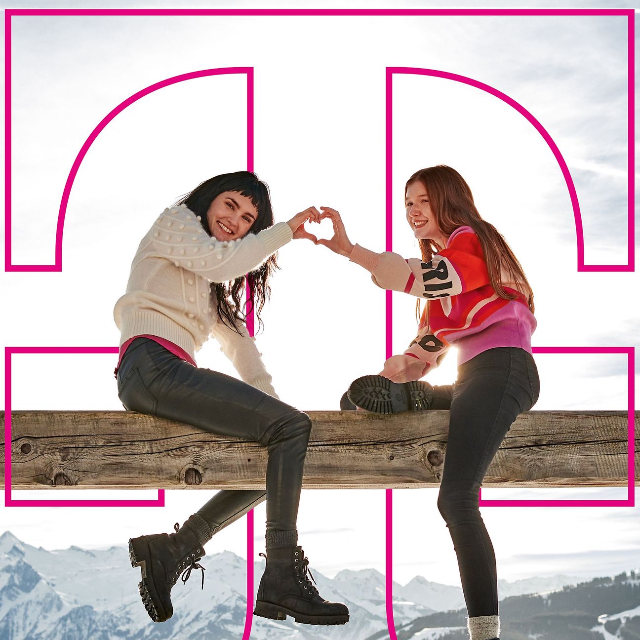 Two young women sit on a beam and form a heart with their hands