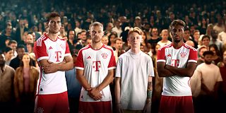 Drei Spieler des FC Bayern München und ein junger Mann stehen vor Fußballfans.