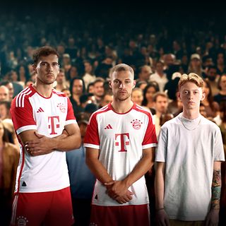 Drei Spieler des FC Bayern München und ein junger Mann stehen vor Fußballfans.