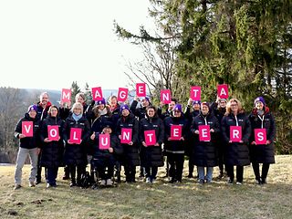 Telekom Mitarbeiterinnen und Mitarbeiter, die den Begriff „Magenta Volunteers“ mit Buchstaben-Schildern in die Luft halten.