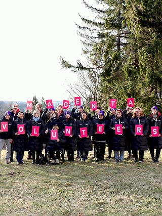 Telekom Mitarbeiterinnen und Mitarbeiter, die den Begriff „Magenta Volunteers“ mit Buchstaben-Schildern in die Luft halten.