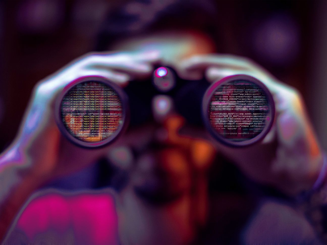shadowy figure looks through binoculars in which lines of code are reflected