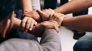 Close-up of five different hands holding each other's wrists, forming a circle