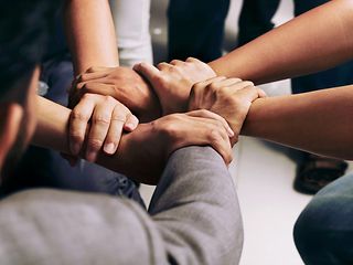 Close-up of five different hands holding each other's wrists, forming a circle