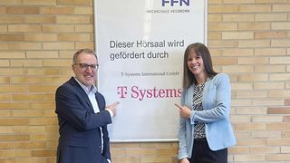 A man and a woman point to a sign that reads, "This lecture hall is funded by <nobr>T-Systems</nobr>."