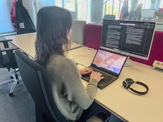 A young woman sits at the desk in front of her laptop