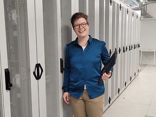 A woman stands in a computer room with a laptop in her arms