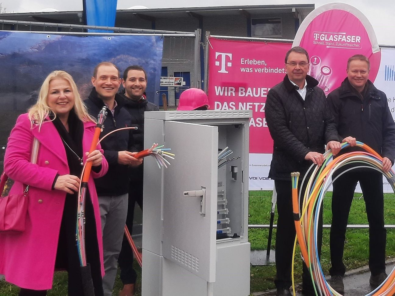 Personen stehen vor einem geöffneten Netzverteiler. Manche halten Abschnitte von Speed Pipes in den Händen. 