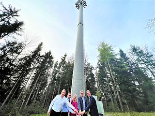 Personen drücken gemeinsam einen Buzzer, im Hintergrund der neue Mobilfunkmast und viele Bäume. 