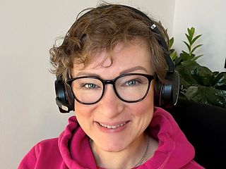 Eine Frau sitzt mit Kopfhörern bei der Arbeit und lächelt in die Kamera