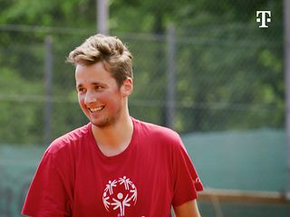 Tennisspieler Louis Kleemeyer lachend in einem roten T-Shirt auf einem Tennisplatz.