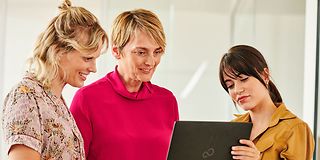 Bild von drei Frauen, die in einen Laptop schauen und diskutieren.
