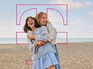 Zwei Frauen umarmen sich an einem sandigen Strand.