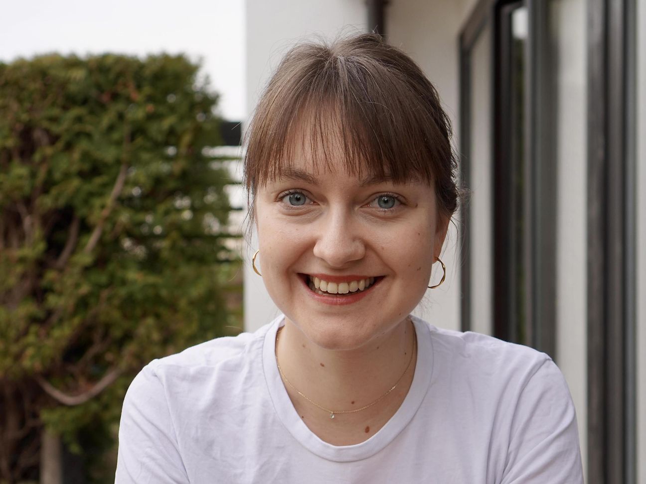 Young woman sitting outside in the greenery and smiling at the camera