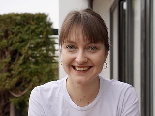 Young woman sitting outside in the greenery and smiling at the camera